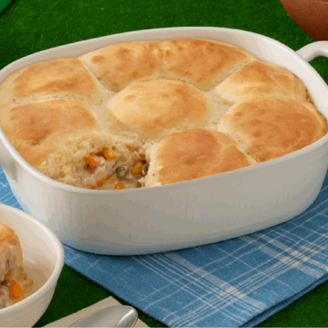 Chicken pot pie in a white casserole dish with a golden biscuit crust, a portion scooped to reveal chicken and vegetable filling.