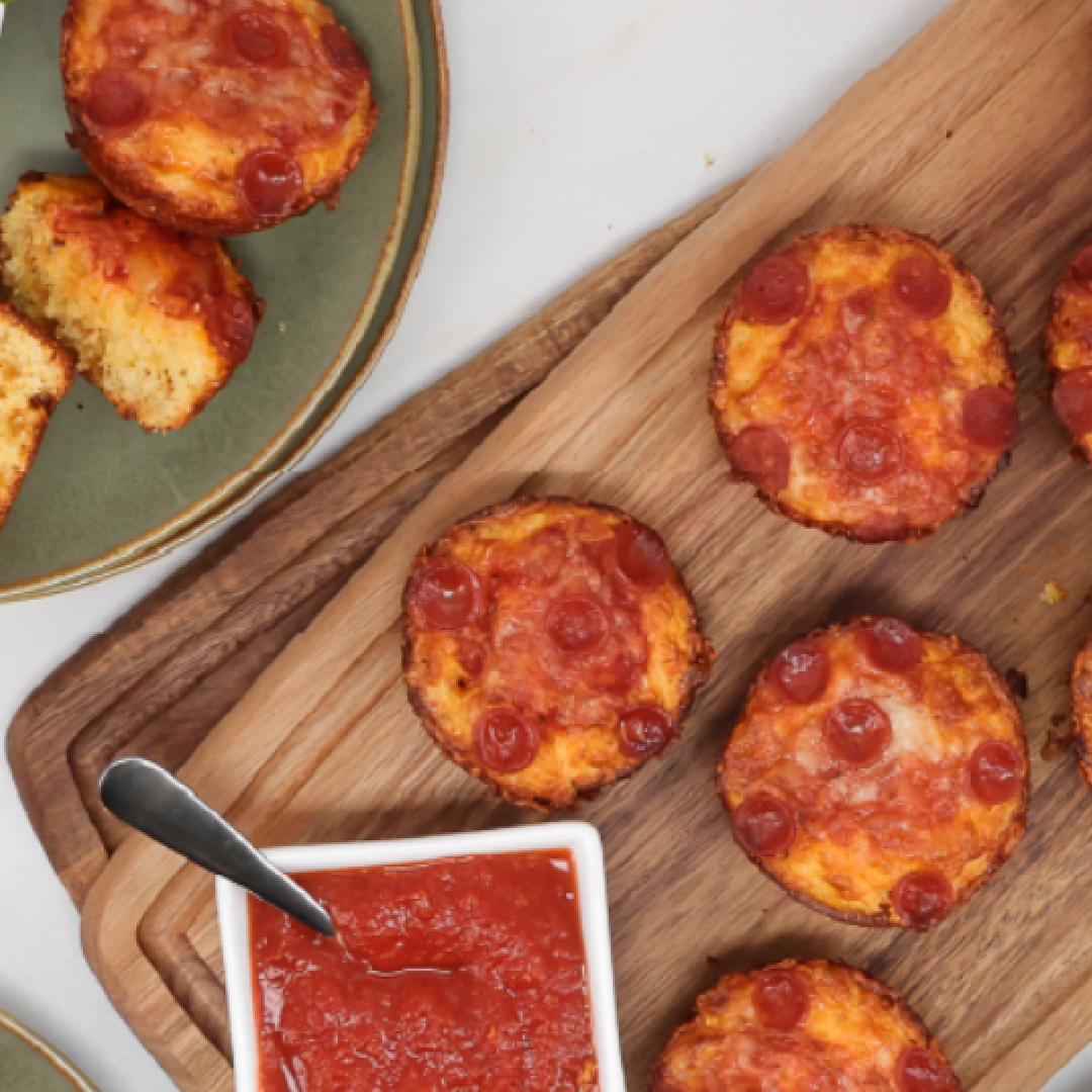 Mini pepperoni pizzas arranged on a wooden board with a bowl of marinara sauce nearby.