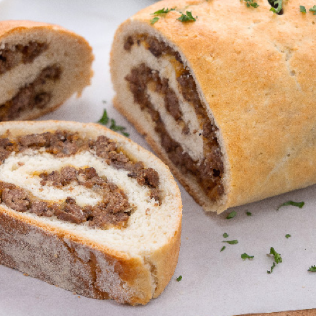 Savory meat-filled swirl bread loaf sliced to reveal a spiral beef filling, sprinkled with herbs.