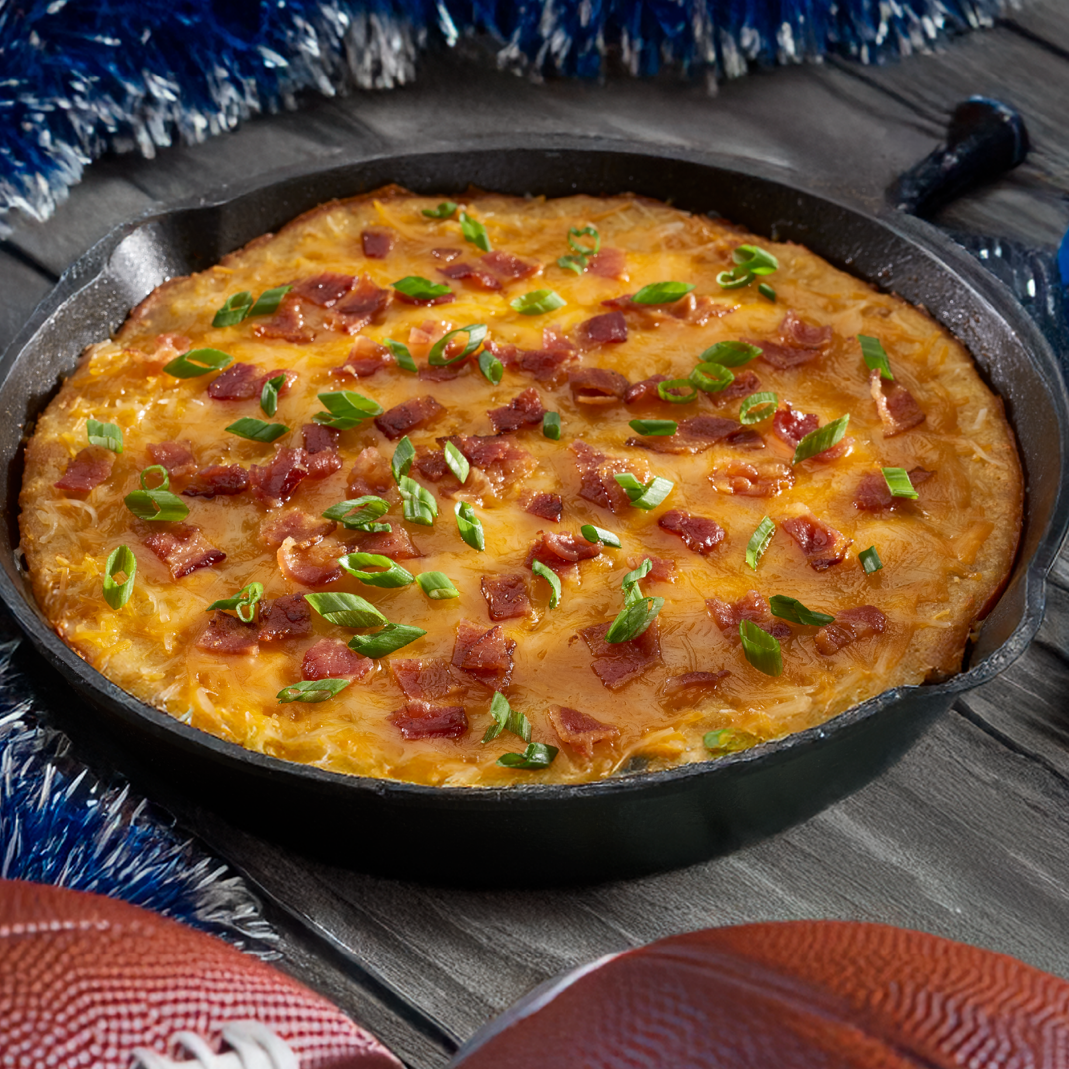 A cheesy bacon and scallion pizza baked in a black cast‑iron skillet on a wooden table, with a crispy crust edge visible.