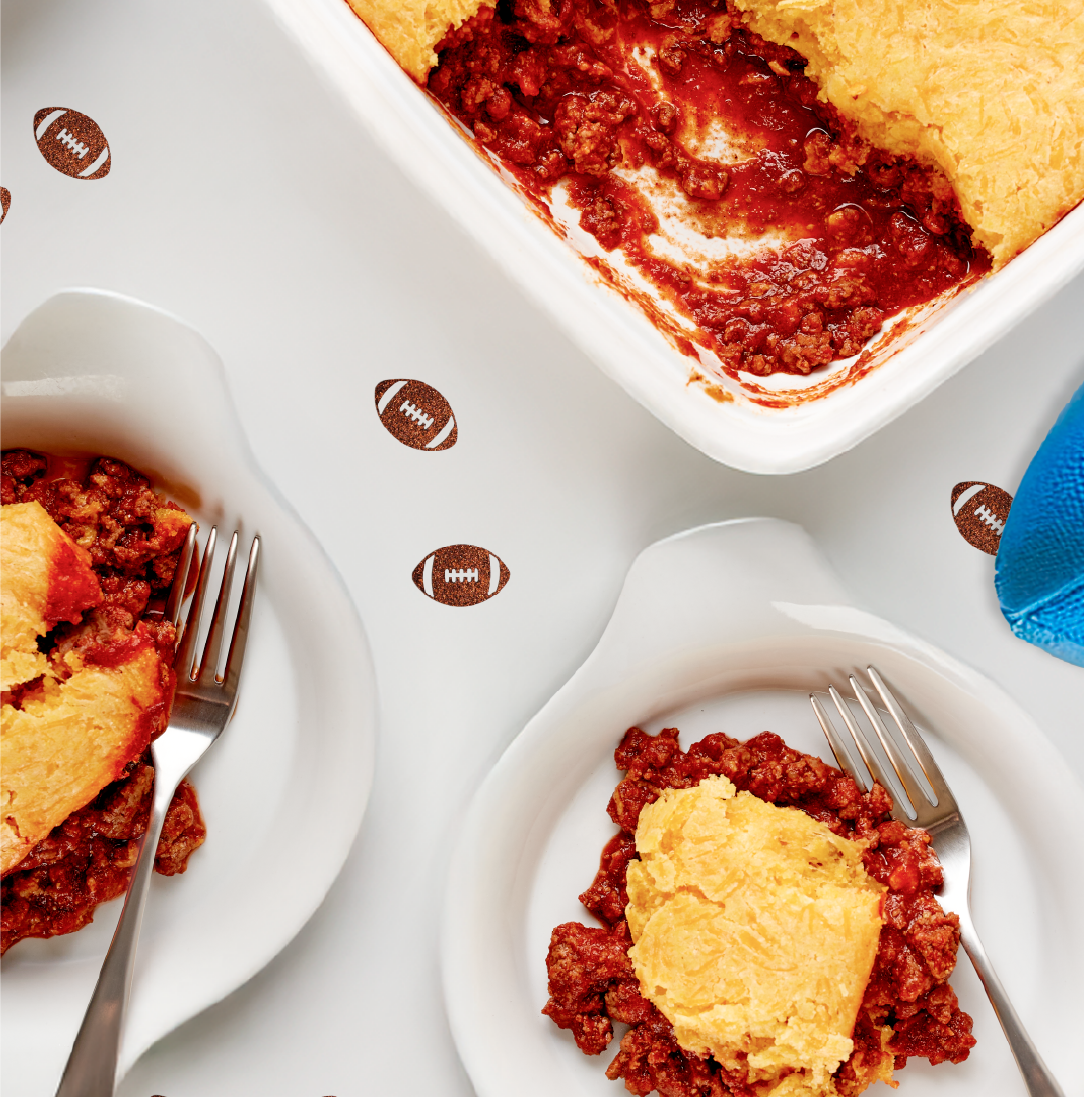 Slices of meat pie with a flaky crust and red filling served on white plates, football-themed table decorations nearby.